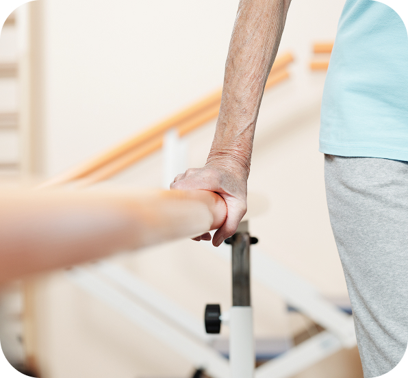 Seniorin hält sich bei Reha-Übungen an einer Gehstange fest.